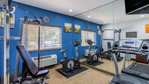 A gym with exercise equipment, a mirrored wall, and a clock.