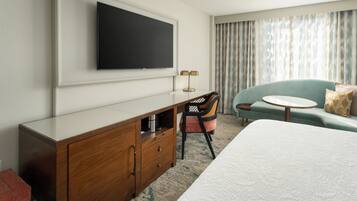 A hotel room with a bed, a desk with a flat-screen TV, a chair, a sofa, and a round table.