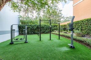 An outdoor gym area with exercise equipment, artificial grass, and a hedge.