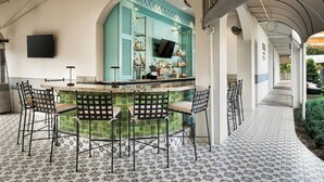 A bar area with a green-tiled counter, black metal chairs, and a television mounted on the wall. - Castle Hotel, Autograph Collection (Orlando)