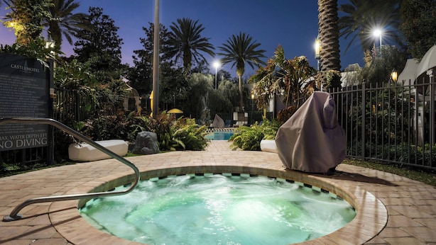 A hot tub surrounded by a brick patio, palm trees, and a fence. - Castle Hotel, Autograph Collection (Orlando)