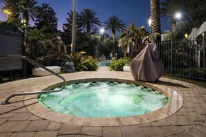 A hot tub surrounded by a brick patio, palm trees, and a fence.