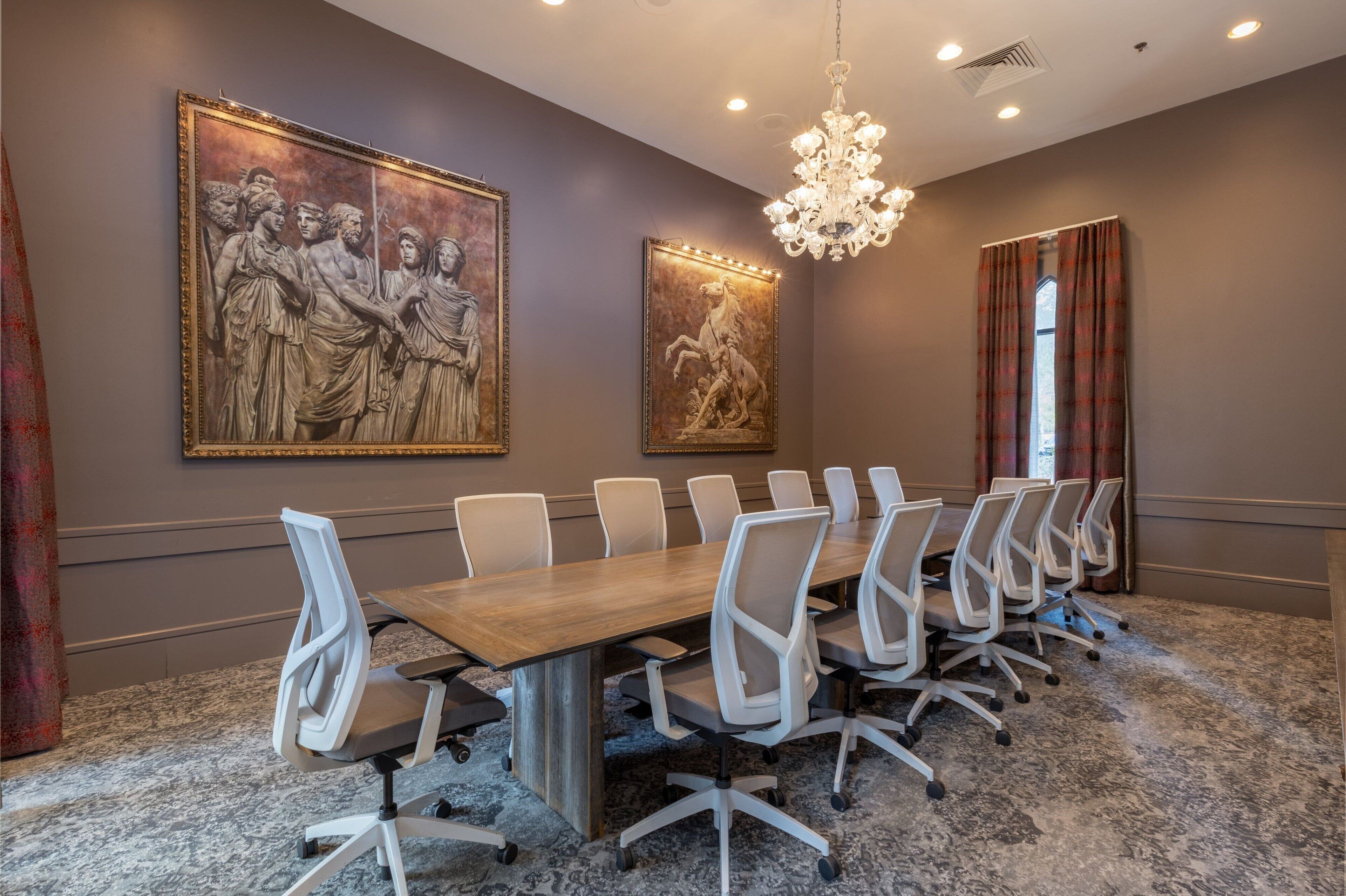 A conference room with a long table, white chairs, and two large classical paintings on the walls.