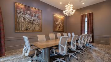 A conference room with a long table, white chairs, and two large classical paintings on the walls.