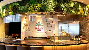 Un restaurante con un mostrador curvo, taburetes de bar, una pared verde con plantas y un letrero que dice 'La Pacifica Restaurant'.