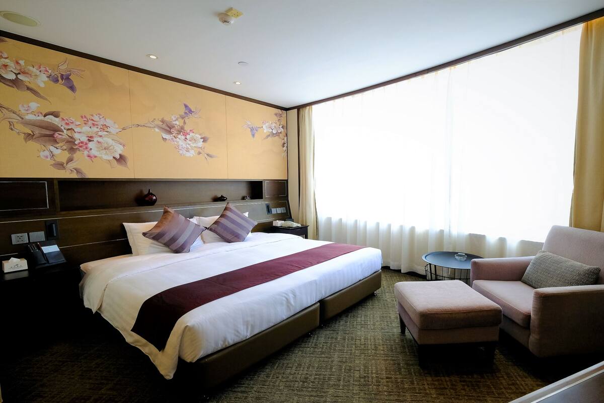 Een hotelkamer met een groot bed, een bank, een klein tafeltje en een wand met bloemenkunst.