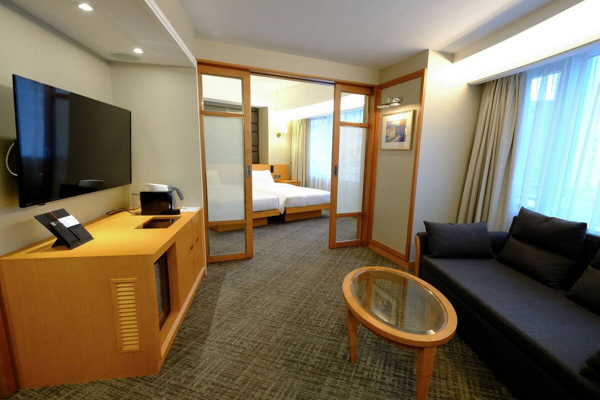 Een hotelkamer met een televisie, een bureau met koffiezetapparaat, een bank, een glazen tafel en een bed met een schuifdeur naar een badkamer.