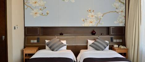 Une chambre d’hôtel avec deux lits, une grande fresque murale à motifs floraux, une tête de lit en bois et une table de chevet avec un téléphone.