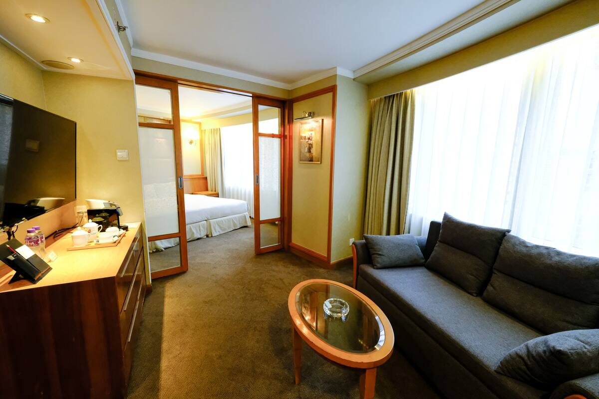 Een hotelkamer met een bank, een glazen salontafel, een bureau met telefoon en een bed.