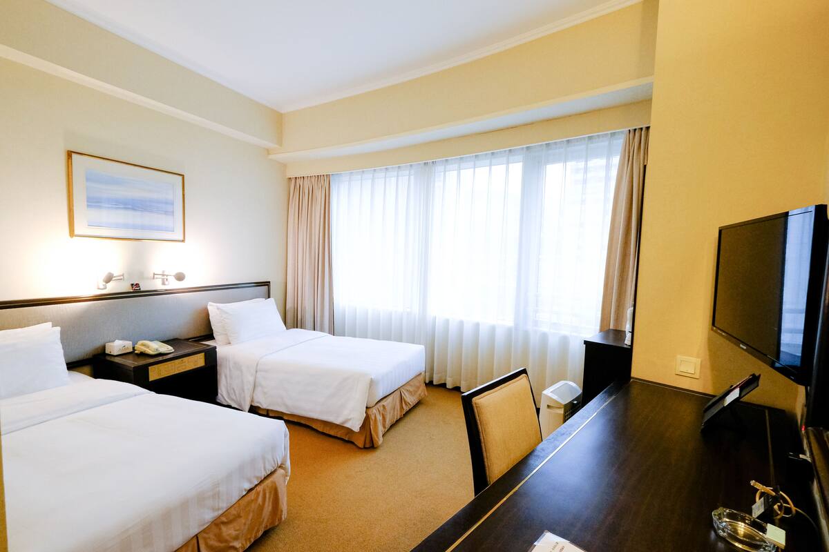 Een hotelkamer met twee bedden, een bureau, een televisietoestel en een raam met gordijnen.