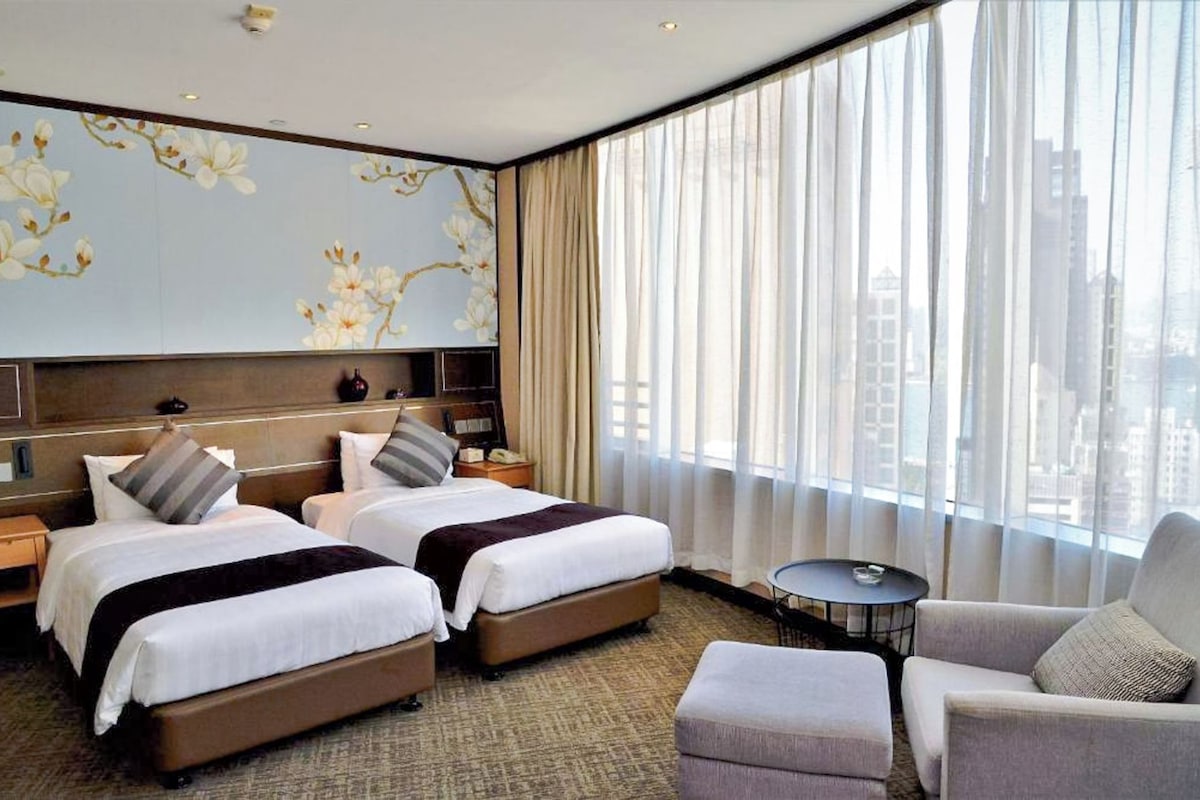A hotel room with two beds, a sitting area, and a large window with curtains.
