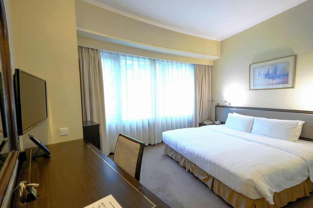 Een hotelkamer met een groot bed, een bureau met stoel, een televisie en een raam met gordijnen.