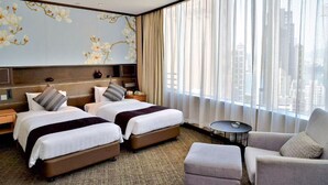 Habitación de hotel con dos camas, un sofá, una mesita y un ventanal grande con cortinas.