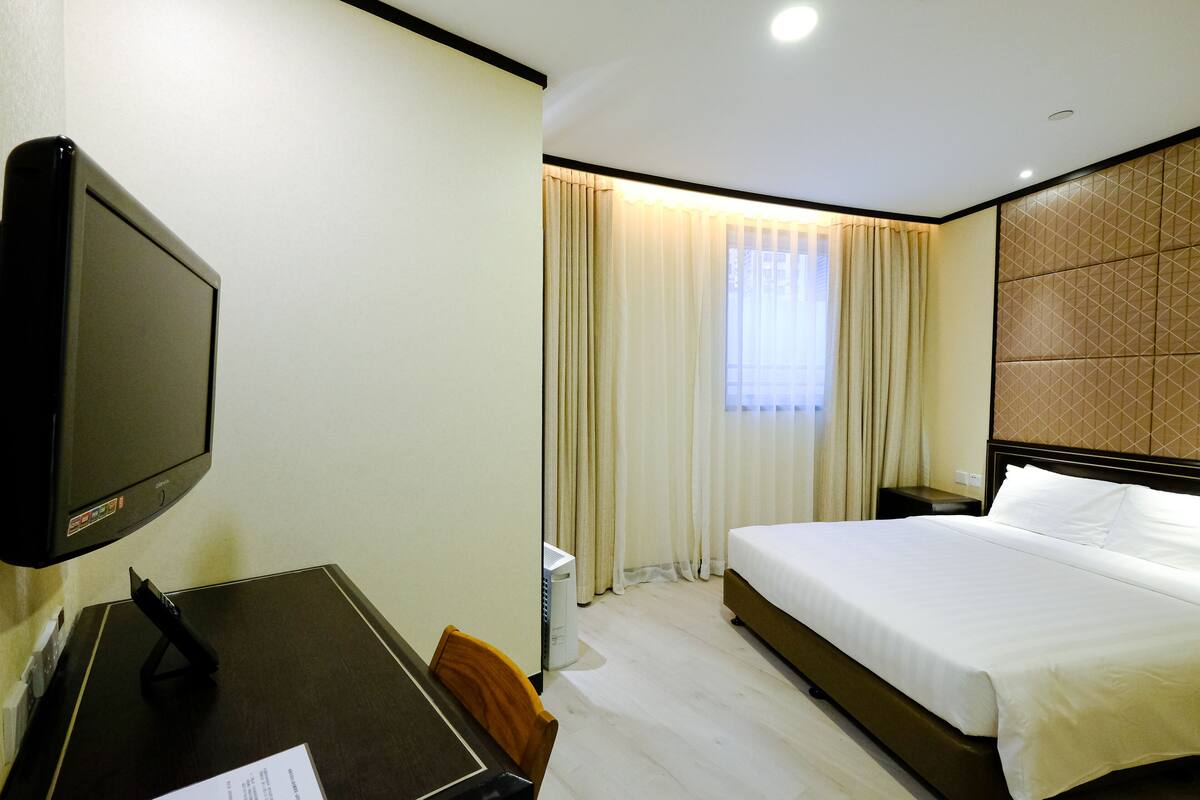 Een hotelkamer met een bed, een bureau met een computer, een televisie en een raam met gordijnen.