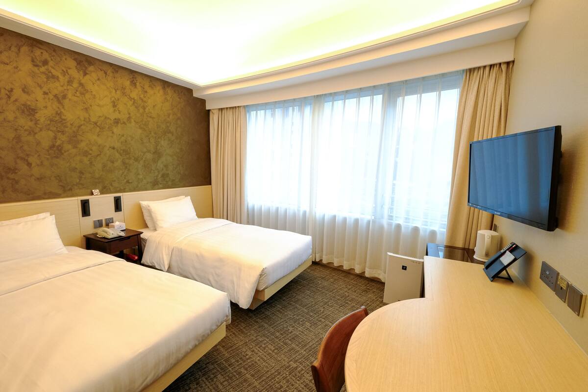 Een hotelkamer met twee bedden, een bureau, een stoel, een televisie en een raam met gordijnen.