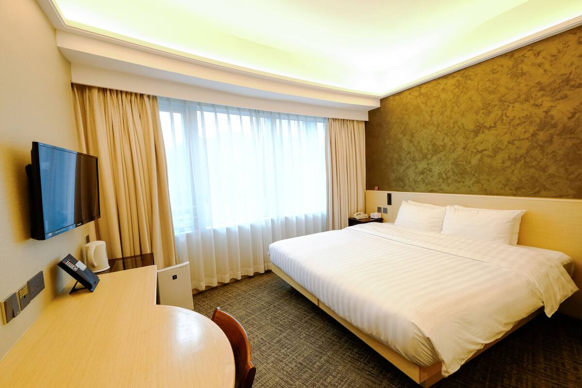 Een hotelkamer met een bed, televisie, bureau en stoel.