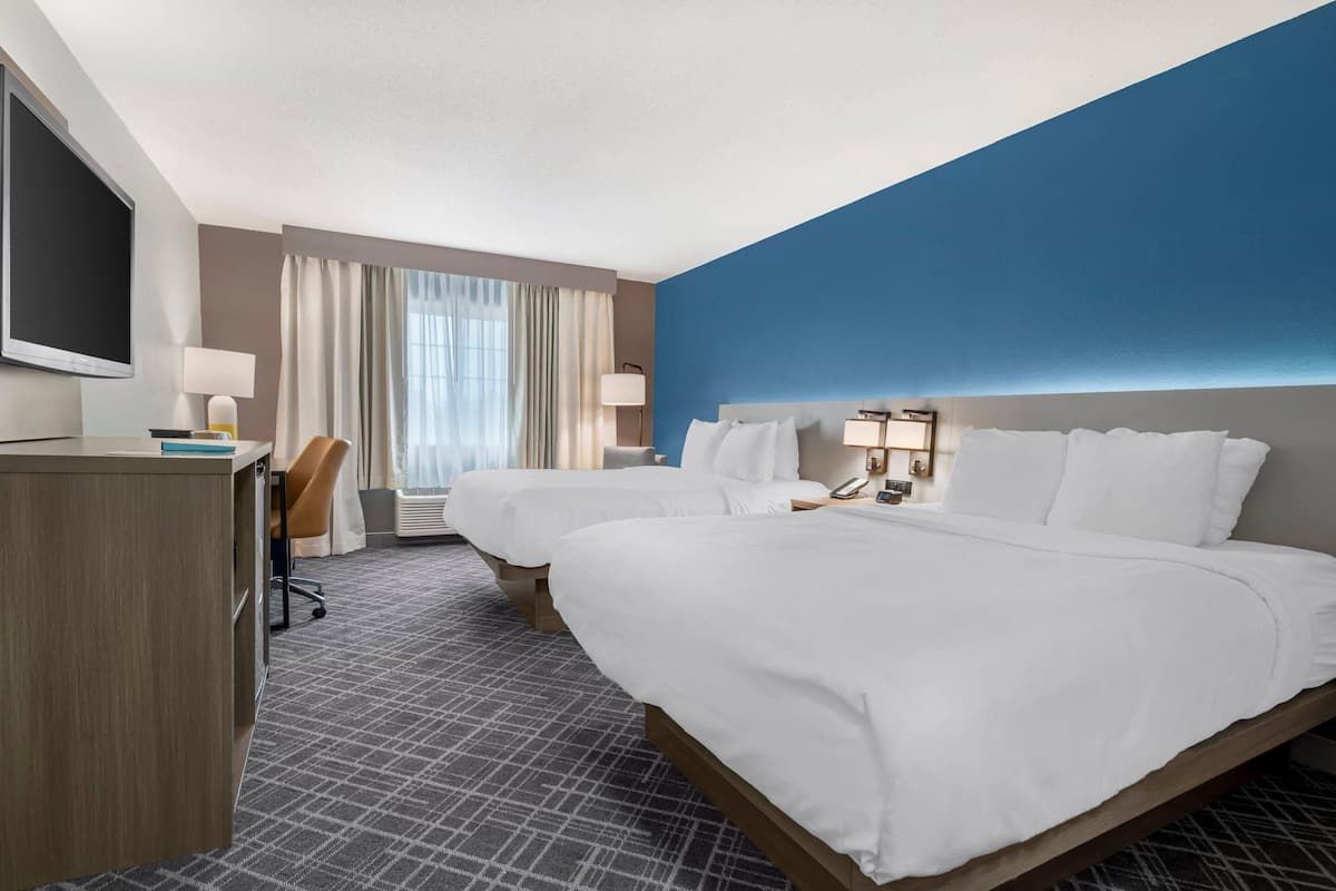 A hotel room with two beds, a desk, a TV, and a window with curtains.