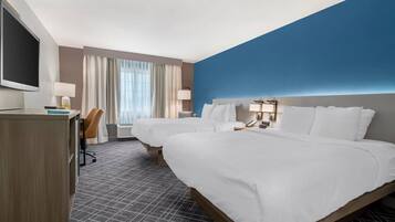 A hotel room with two beds, a desk, a TV, and a window with curtains.