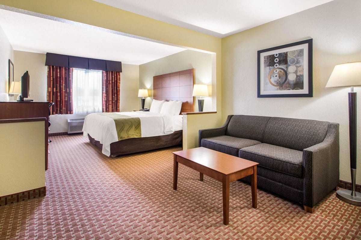 A hotel room with a bed, a sofa, a table, and a lamp.