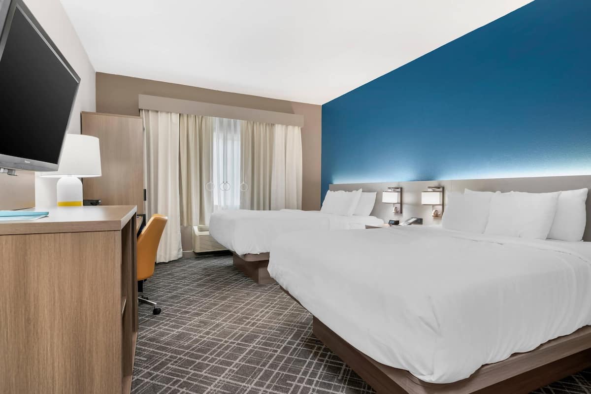 A hotel room with a large bed, a desk with a TV, a chair, and a window with curtains.