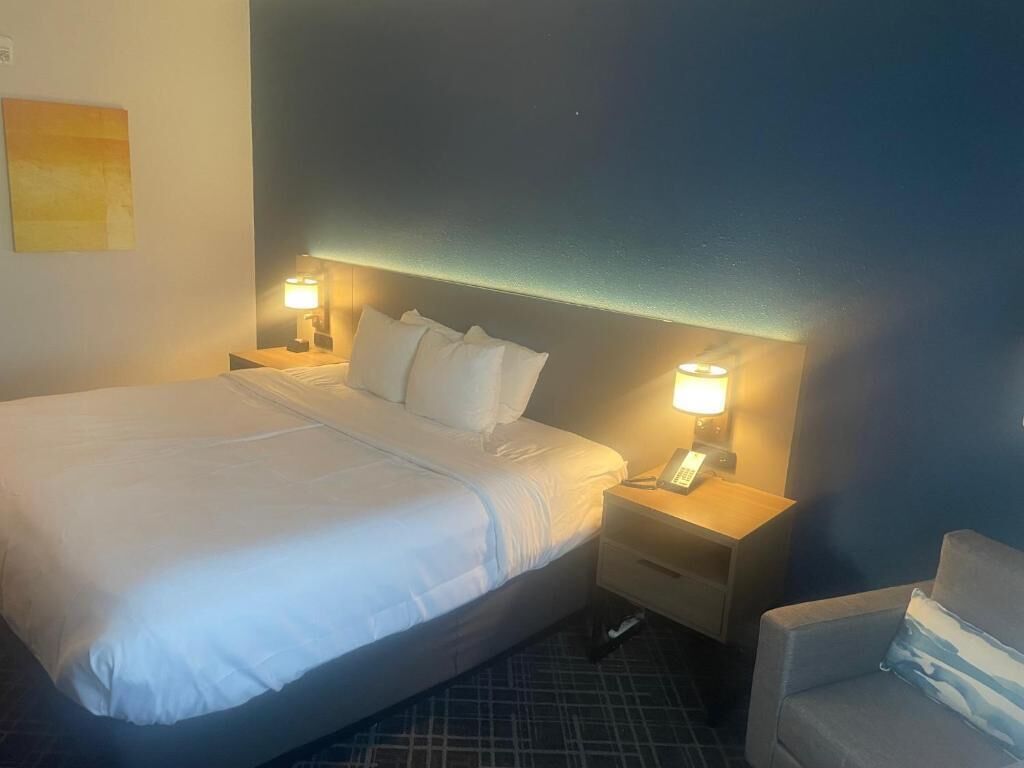 A hotel room with a large bed, bedside lamps, a nightstand, a chair, and a wall-mounted telephone.