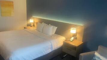 A hotel room with a large bed, bedside lamps, a nightstand, a chair, and a wall-mounted telephone.