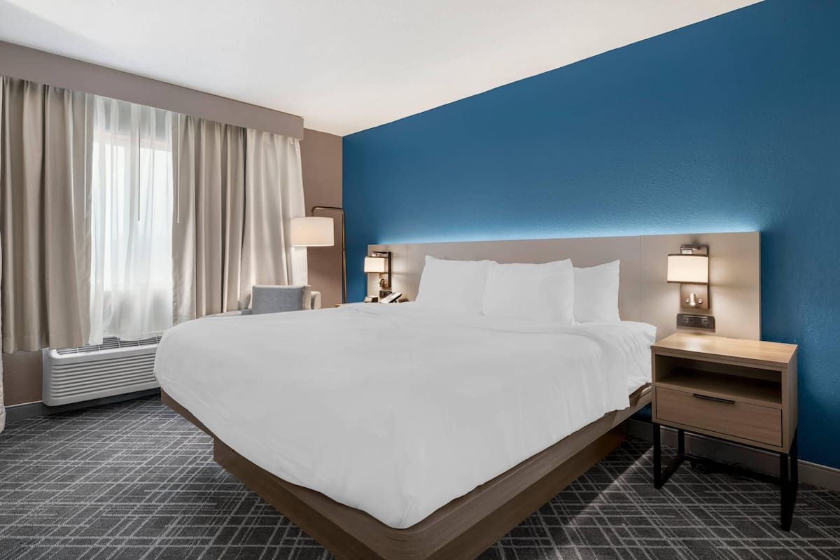 A hotel room with a large bed, two bedside tables with lamps, a heater, and a window with curtains.