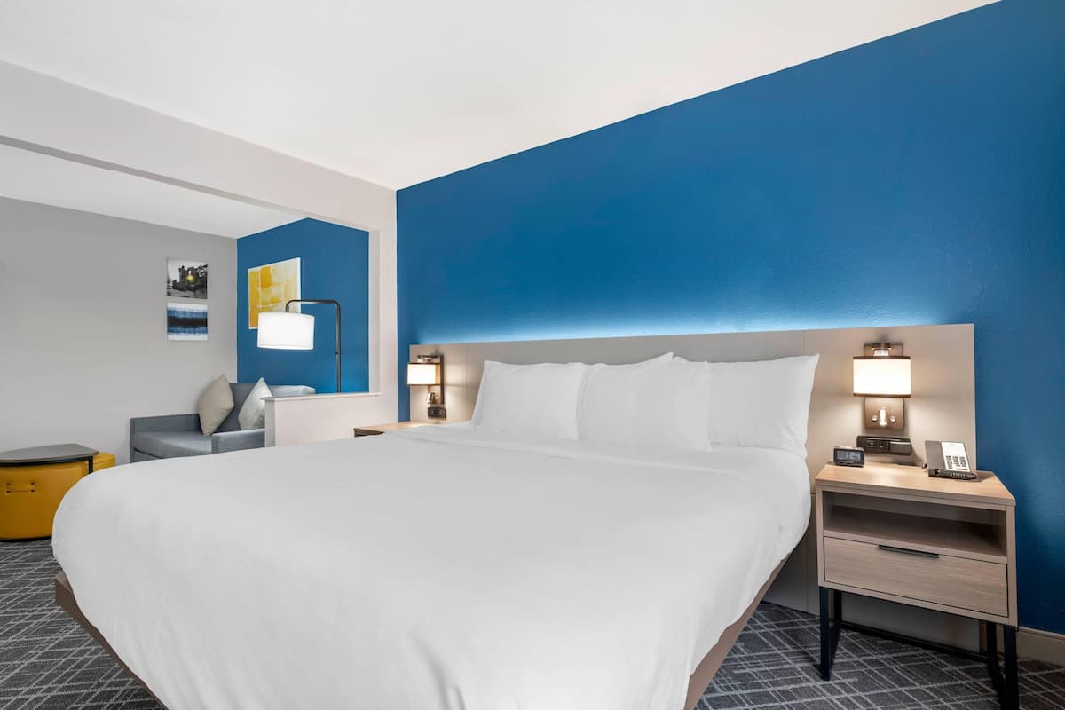 A hotel room with a large bed, bedside tables, a chair, and a small desk.