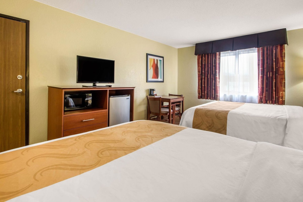 A hotel room with two beds, a desk, a television, and a window with curtains.