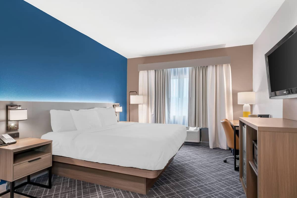 A hotel room with a bed, bedside table, lamp, desk, chair, and TV.