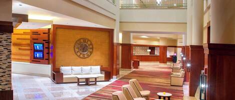 A spacious hotel lobby with a high ceiling, multiple seating areas, and a large clock on the wall.