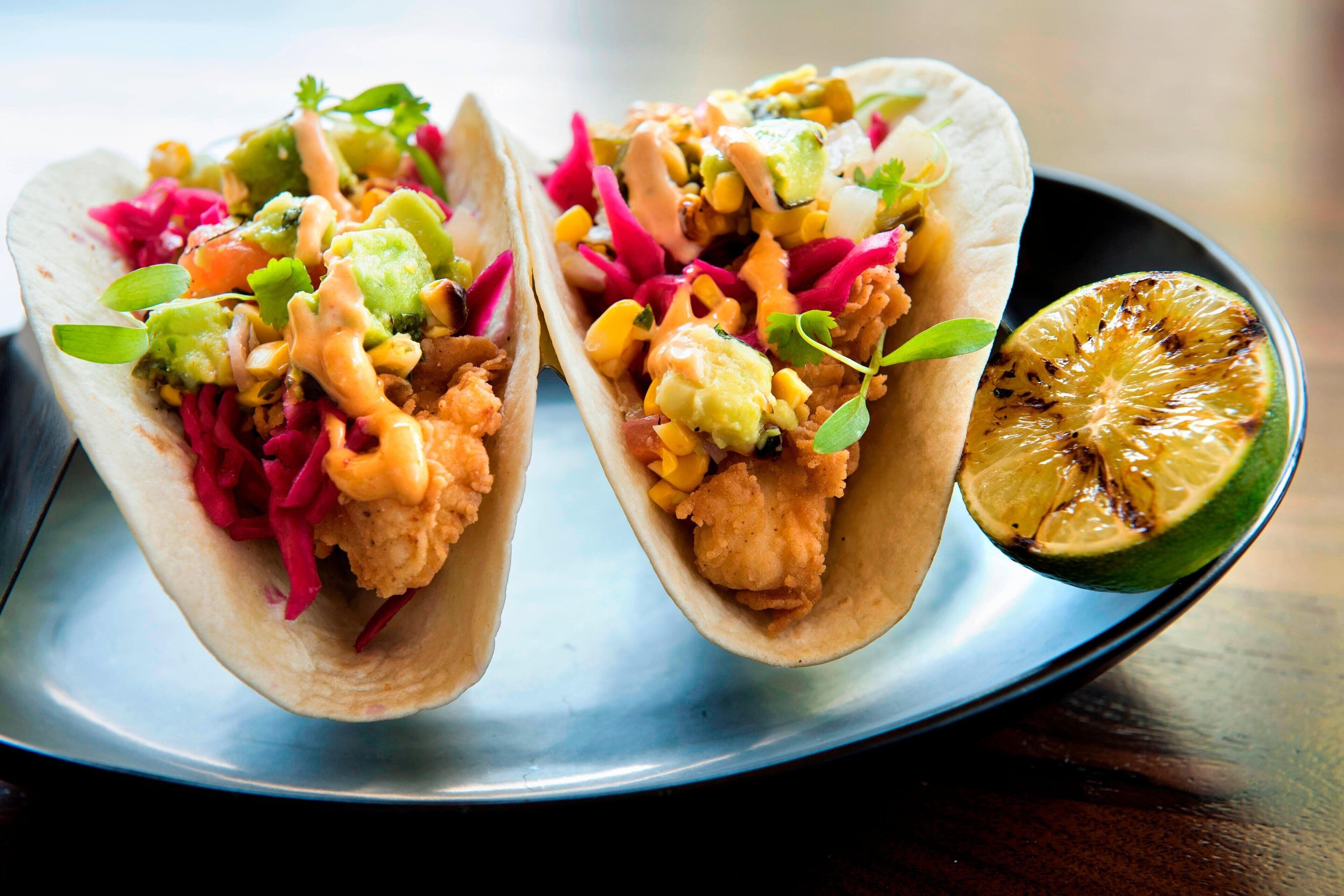 Two tacos on a metal plate with a slice of grilled lime.