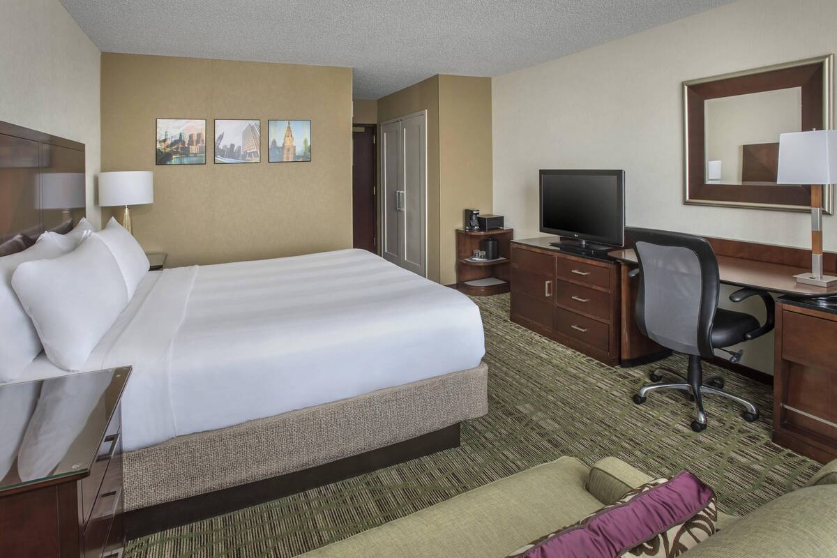 Una habitación de hotel con una cama grande, un escritorio con una computadora, un televisor y un armario.