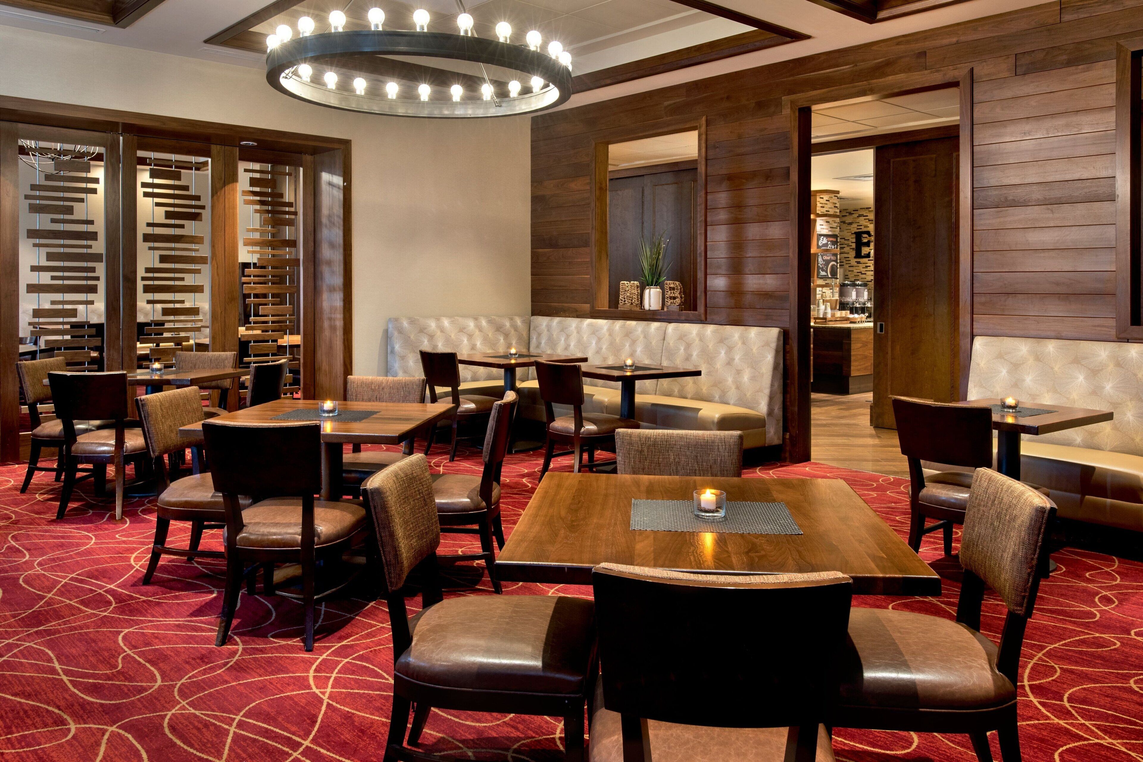 Un hall d’hôtel doté de plusieurs espaces de détente, comprenant des tables et des banquettes, et recouvert d’un tapis rouge à motifs.