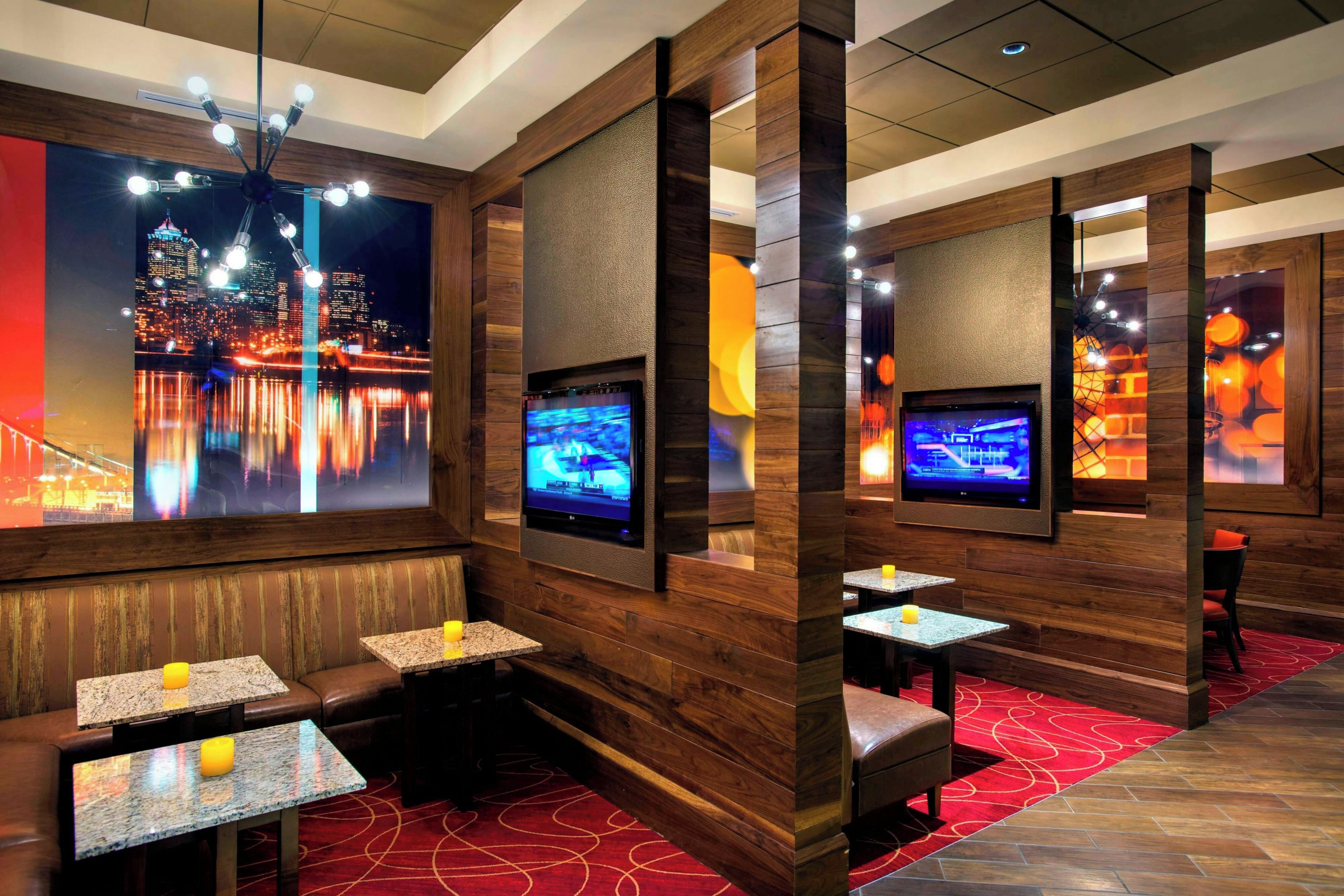 A modern interior with wooden paneling, multiple screens, seating areas, and a red carpeted floor.
