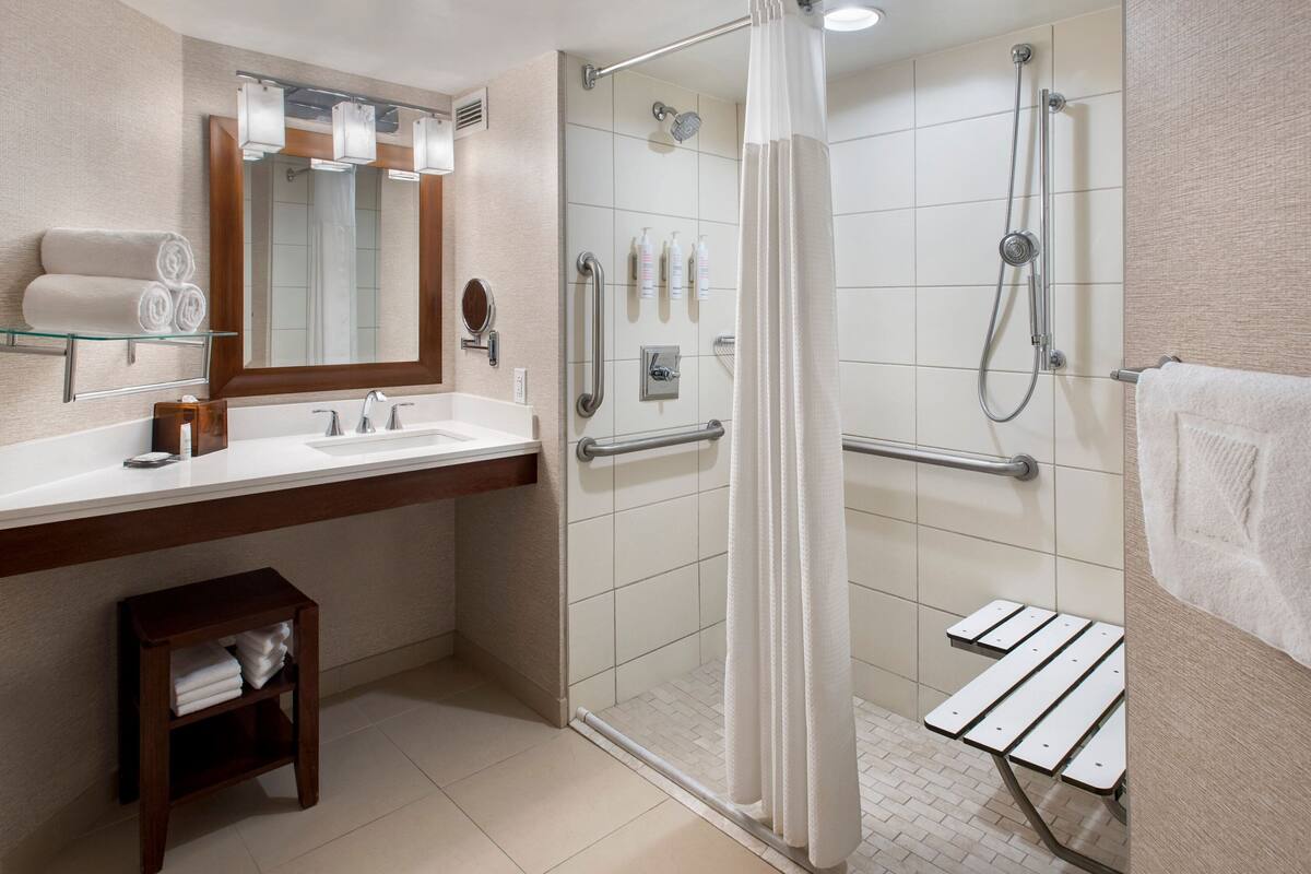 Un baño moderno con cabina de ducha de vidrio, tocador con espejo y un pequeño taburete de madera.