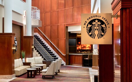 A hotel lobby with a staircase, seating area, and a Starbucks logo.