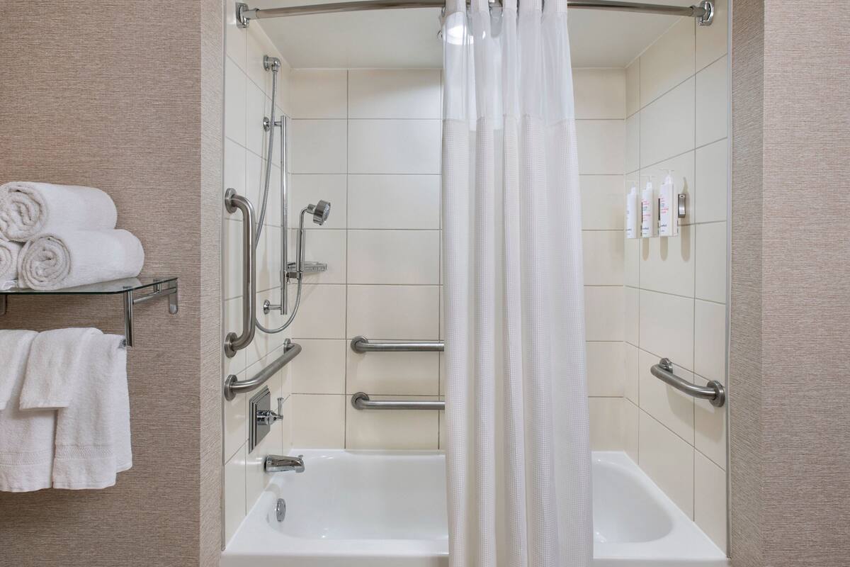 Un baño moderno con ducha, bañera e inodoro. Cuenta con barras de apoyo y un asidero para mayor seguridad.