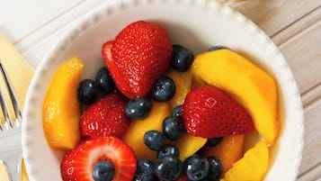 Un tazón de fruta con fresas, arándanos y melocotones, junto a un vaso de jugo de naranja sobre una superficie blanca.