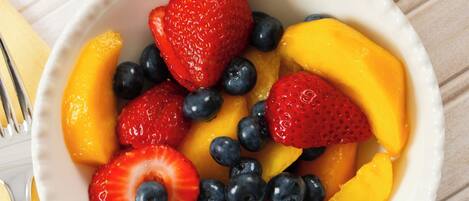 A bowl of fruit with strawberries, blueberries, and peaches, accompanied by a glass of orange juice on a white surface.