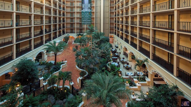 A hotel atrium with multiple floors, a central courtyard with palm trees, and a sign reading "Welcome to the Four Points by Sheraton Tampa Airport Westshore." - Four Points by Sheraton Suites Tampa Airport Westshore (Tampa)
