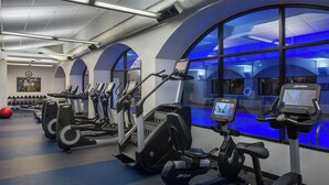 A gym with various cardio machines, a large window with blue lighting, and a wall-mounted TV. - Four Points by Sheraton Suites Tampa Airport Westshore (Tampa)