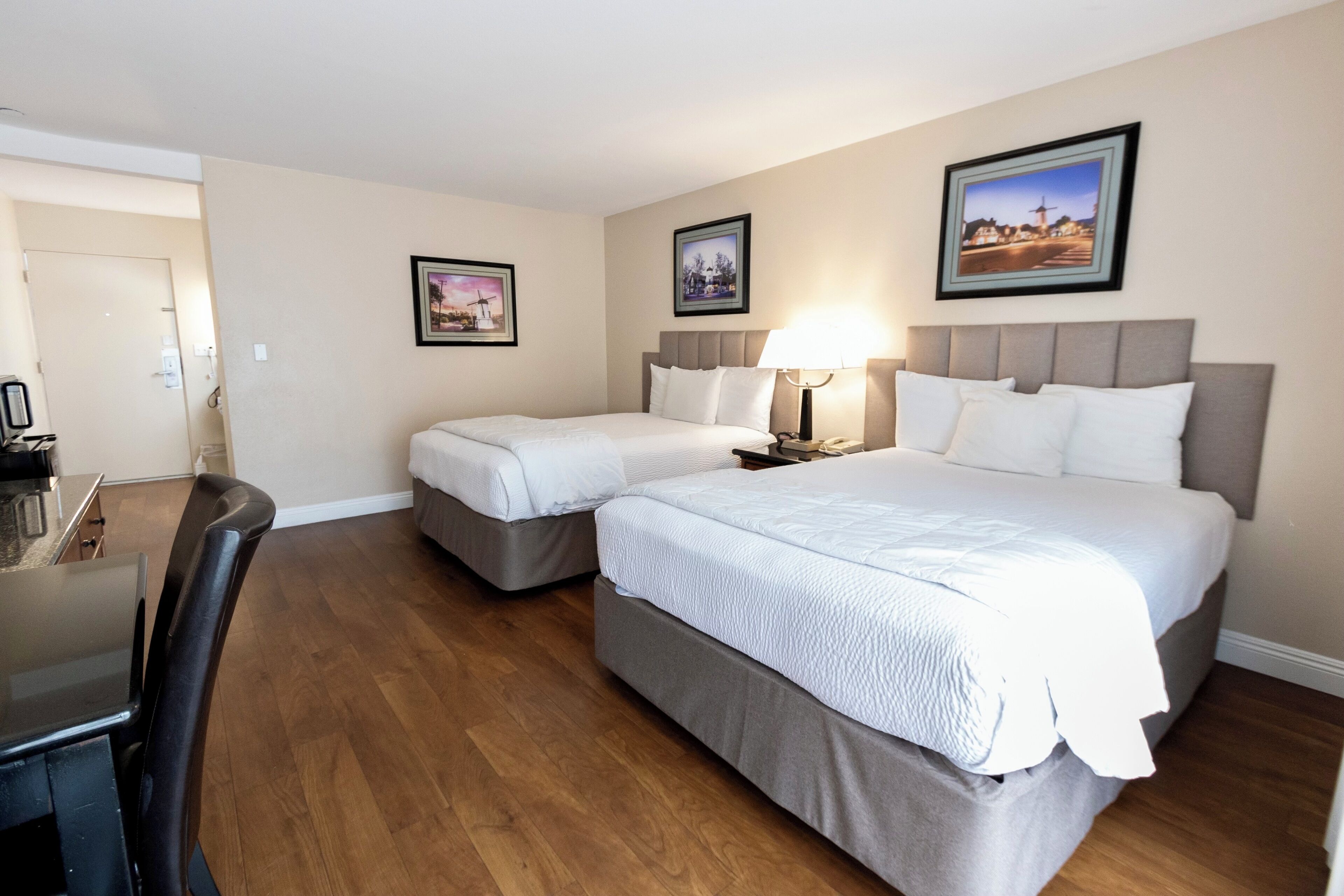 A hotel room with two beds, a desk, and a chair. There are framed pictures on the walls.