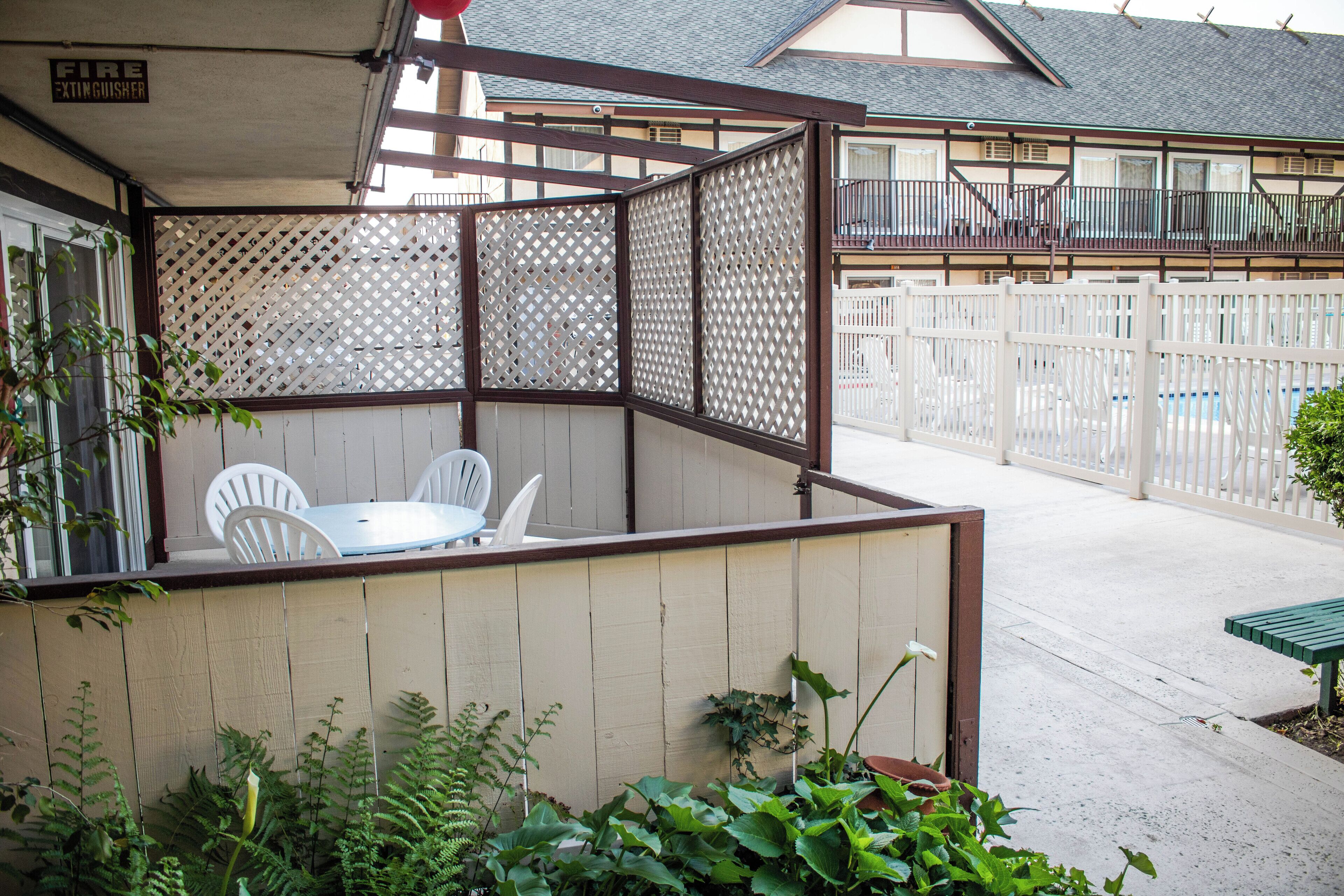 Ein überdachter Patio-Bereich mit Tisch und Stühlen, umgeben von einem Holzzaun und Pflanzen.