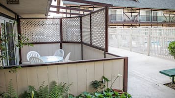 Ein überdachter Patio-Bereich mit Tisch und Stühlen, umgeben von einem Holzzaun und Pflanzen.
