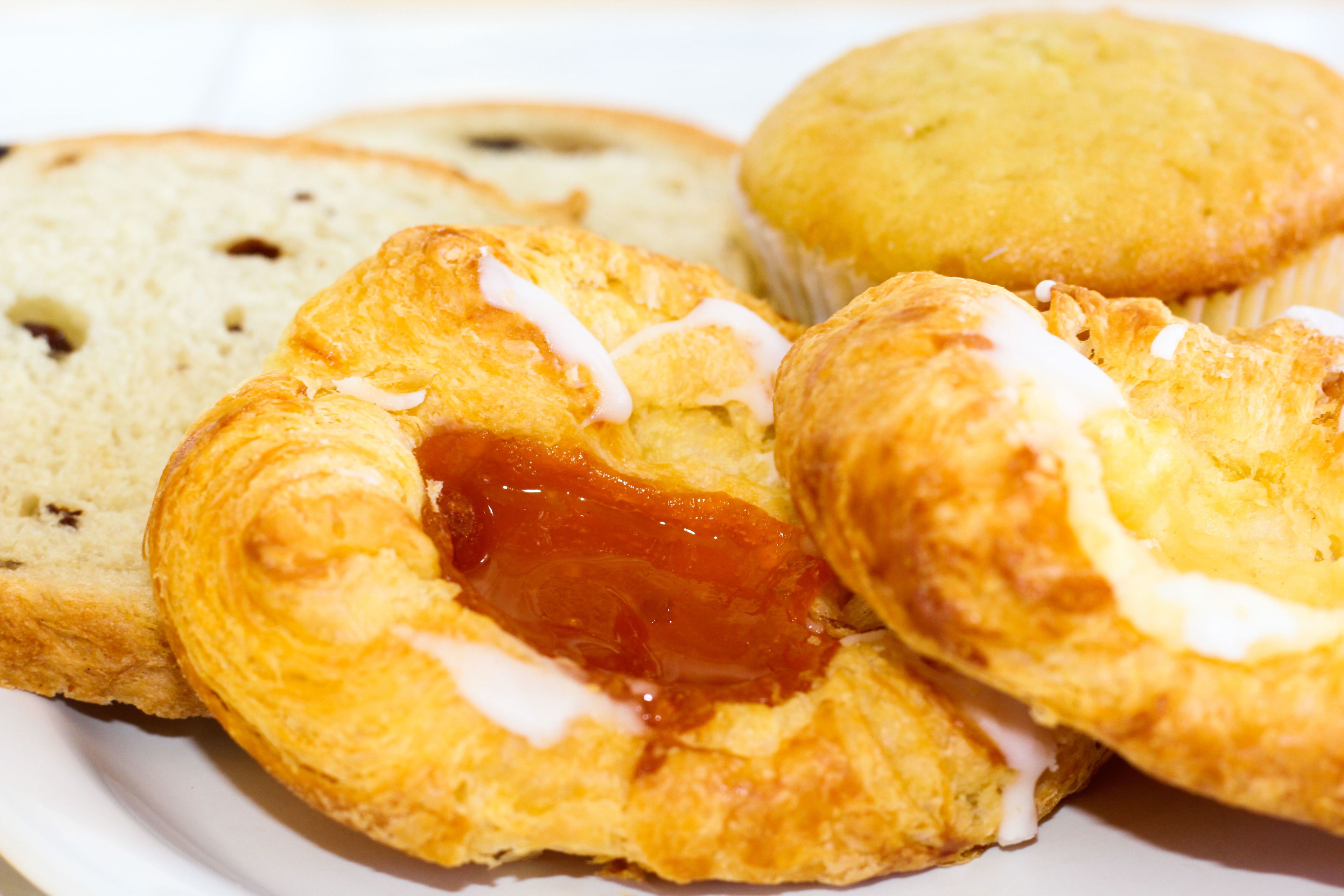 A plate of pastries including a croissant and a muffin with jam and icing.
