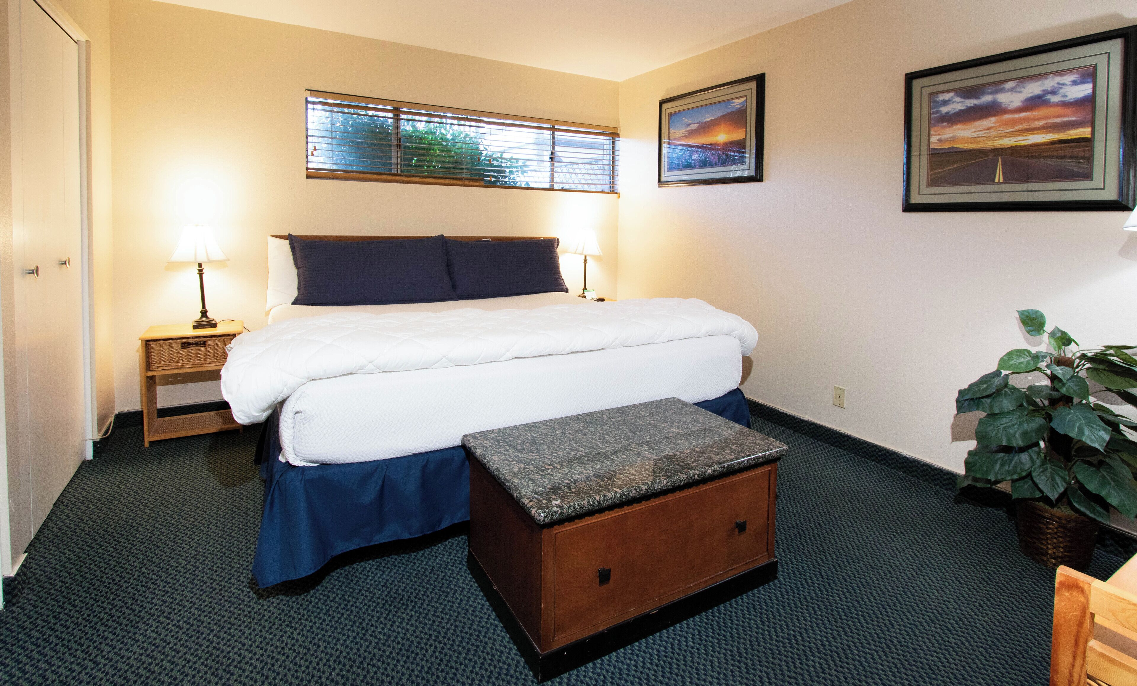 Quarto de hotel com cama, mesas de cabeceira, persianas na janela e um quadro na parede.