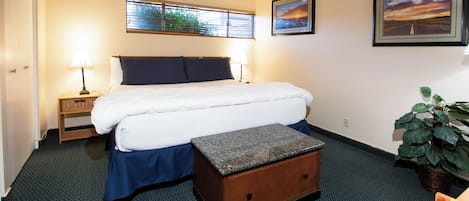 A hotel room with a bed, bedside tables, a nightstand, a window with blinds, and a framed picture on the wall.