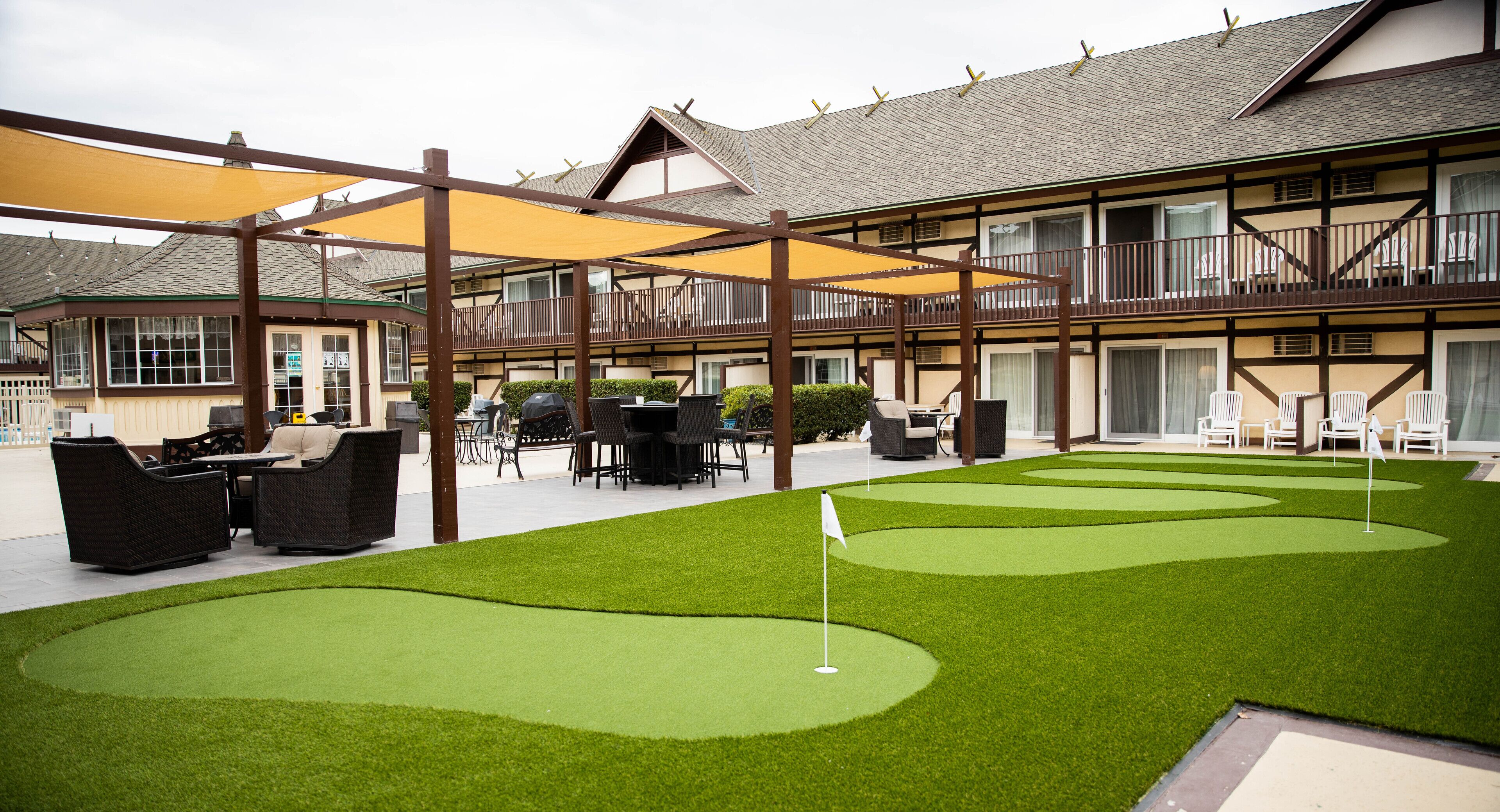 A hotel with a courtyard featuring artificial green grass, a putting green, outdoor seating, and a covered patio area.