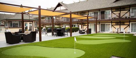 A hotel with a courtyard featuring artificial green grass, a putting green, outdoor seating, and a covered patio area.